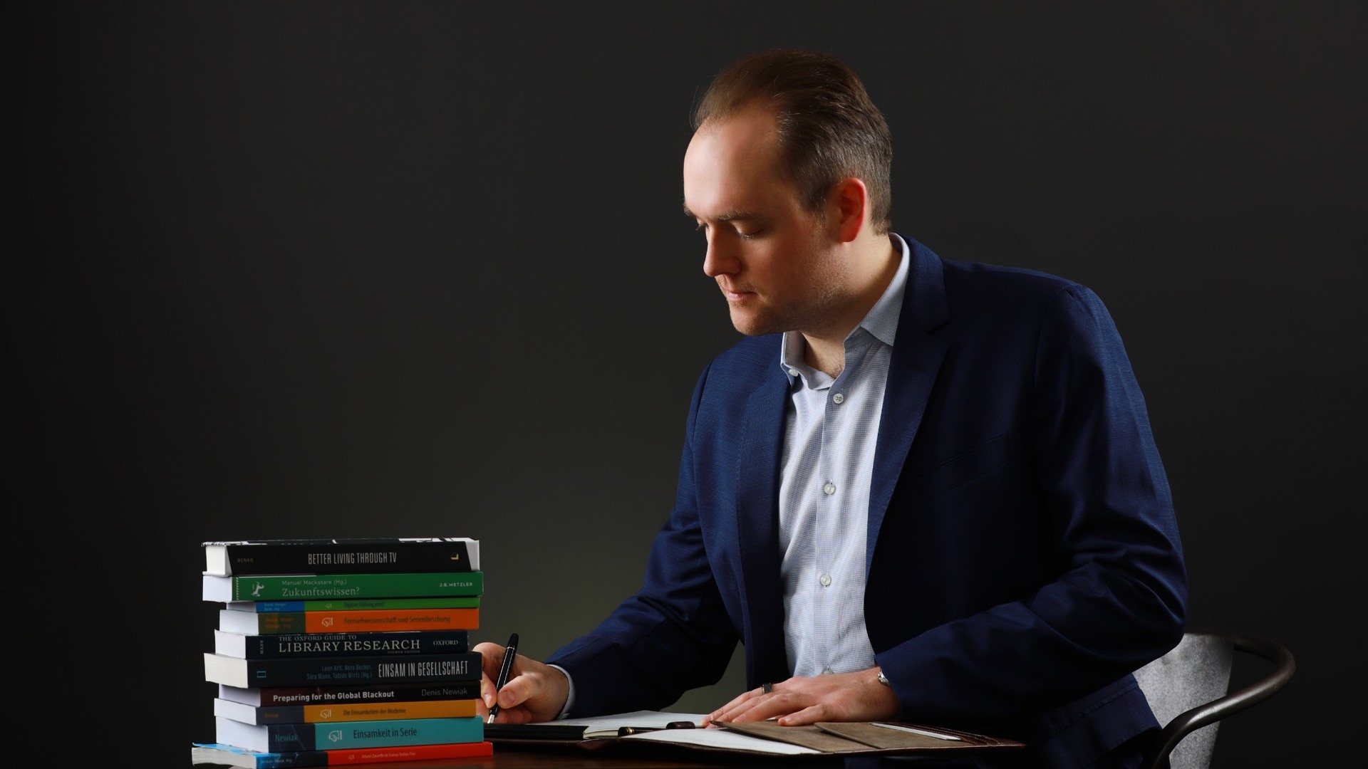 Atelieraufnahme am Schreibtisch mit Büchern und Notizbuch.